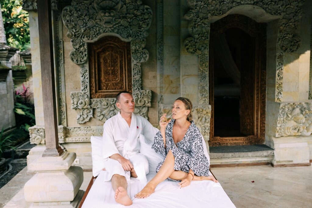 pexels-photo-4965913-4965913 A couple in robes enjoy a relaxing moment outside a Balinese villa with ornate carvings.